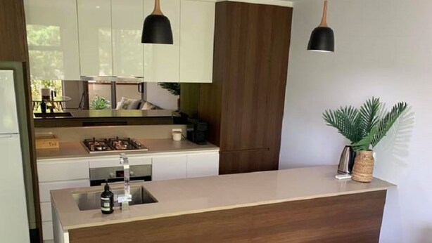 Eine moderne Küche mit einer zentralen Kochinsel, einem Essbereich mit einer schwarzen Ledersofa und einem kleinen runden Tisch mit einer Pflanze.