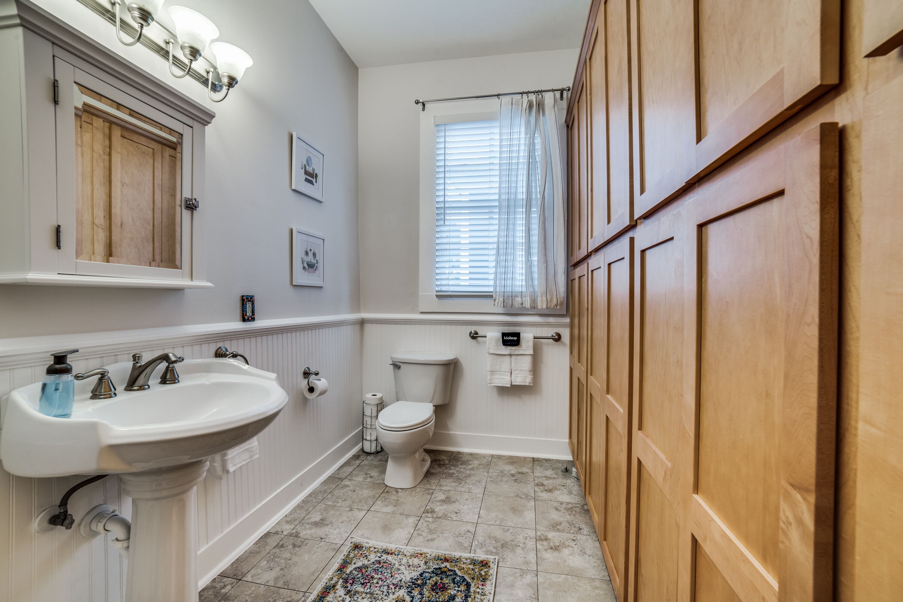 A bathroom with a pedestal sink, toilet, and wooden cabinets.