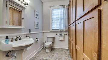 A bathroom with a pedestal sink, toilet, and wooden cabinets.