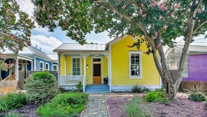 Une maison jaune avec un porche, un chemin de pierres et un arbre aux fleurs roses.