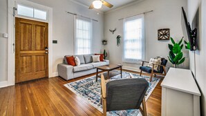 Un salon doté de planchers en bois franc, d’un ventilateur de plafond, d’un canapé, d’une table basse et d’un téléviseur fixé au mur.