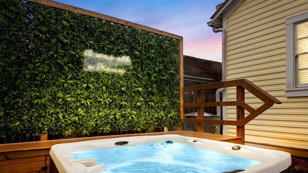 Un bain à remous doté d’une terrasse en bois et d’un mur végétal luxuriant, agrémenté d’une enseigne lumineuse au néon.