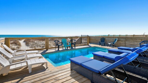 A wooden deck with a pool and lounge chairs overlooking the beach. - Beachfront Duplex | Shared Heated Pool | Pet Friendly (Gulf Shores)