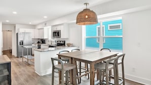 A modern kitchen with white cabinets, stainless steel appliances, and a central island with bar stools. - Beachfront Duplex | Shared Heated Pool | Pet Friendly (Gulf Shores)