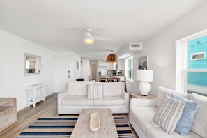 A modern living room with a white sofa, a wooden coffee table, and a kitchen in the background.