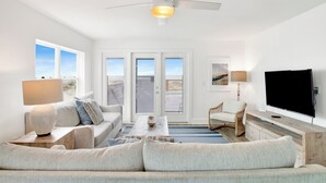 A modern living room with a sofa, a coffee table, a TV, and a ceiling fan. - Beachfront Duplex | Shared Heated Pool | Pet Friendly (Gulf Shores)