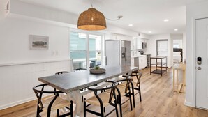 A modern kitchen with a long island, bar stools, a hanging light fixture, and a view of the outdoors.