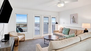 A modern living room with a large window, a ceiling fan, and a flat-screen TV.