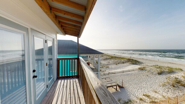 Een pand aan het strand met een houten terras, een overdekt gedeelte met een blauw dak en uitzicht op de oceaan.