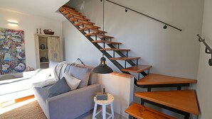 A modern living space with a staircase, a sofa, a small stool, and a table.