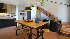 A modern kitchen with a wooden table, black pendant lights, and a vase with green plants.