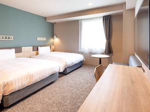 Une chambre d’hôtel avec deux lits, une petite table ronde, une télévision et une fenêtre avec des rideaux.