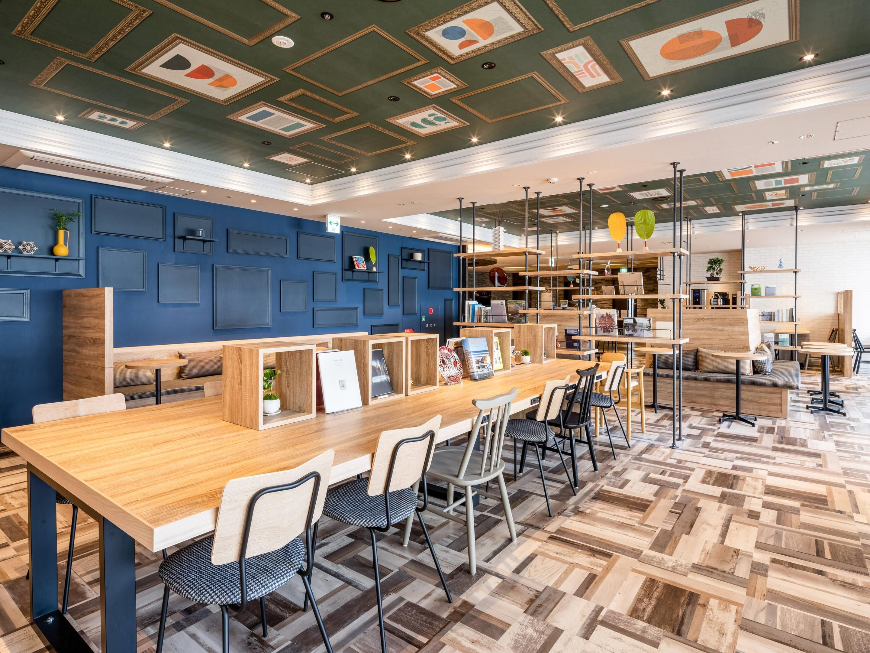 Un interior moderno con una larga mesa de madera, sillas negras y una pared azul con diseños geométricos.
