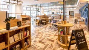 A modern library cafe with wooden furniture, bookshelves, and a sign indicating a welcome drink service. - Comfort Hotel Takamatsu (Takamatsu)