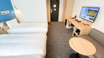 Une chambre d’hôtel avec deux lits, un bureau équipé d’un ordinateur et d’une chaise, une table ronde et un téléviseur fixé au mur.