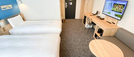 A hotel room with two beds, a desk with a computer and chair, a round table, and a TV on the wall.