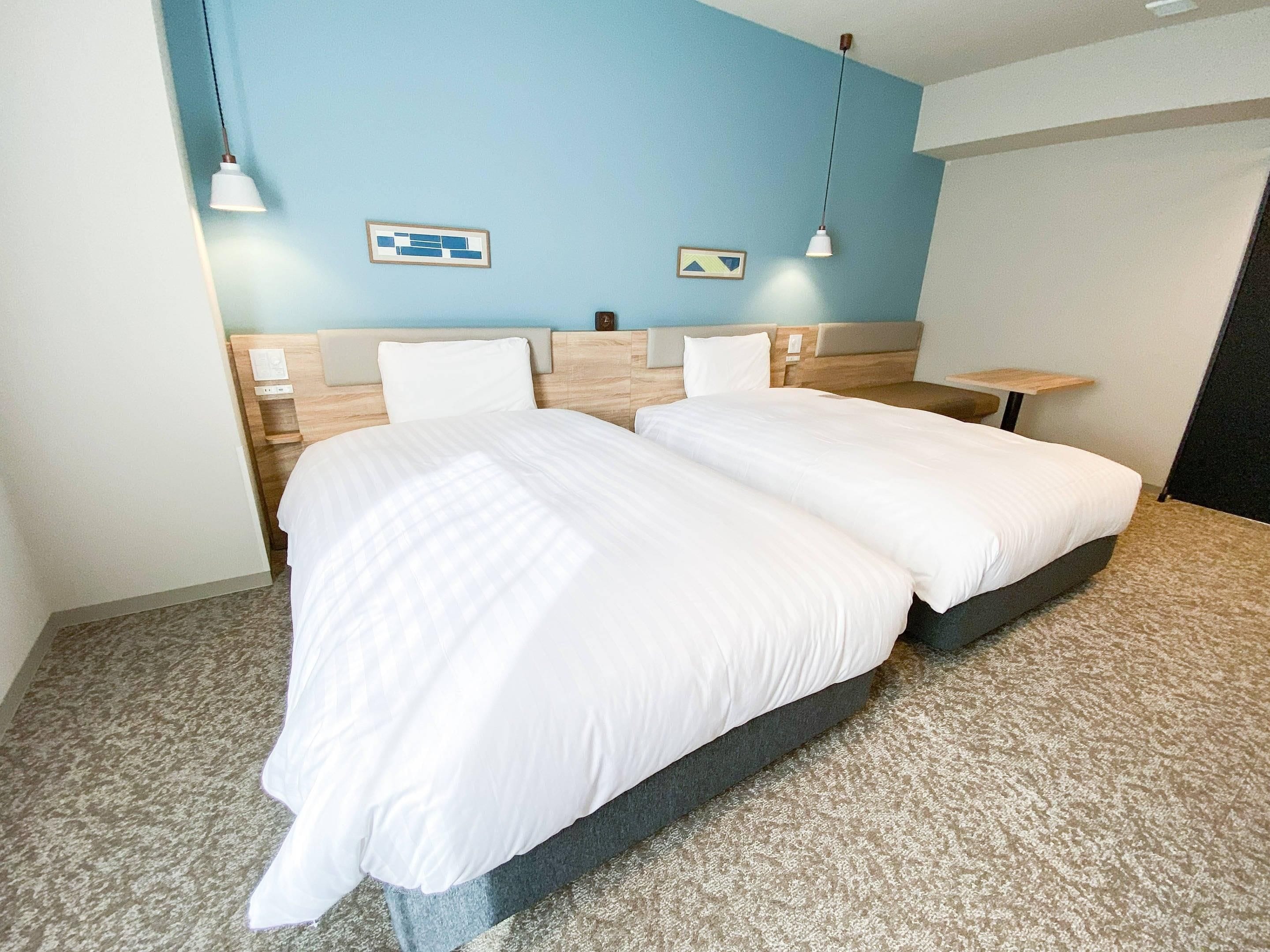 A hotel room with a double bed, two bedside tables, a headboard, and a blue accent wall.