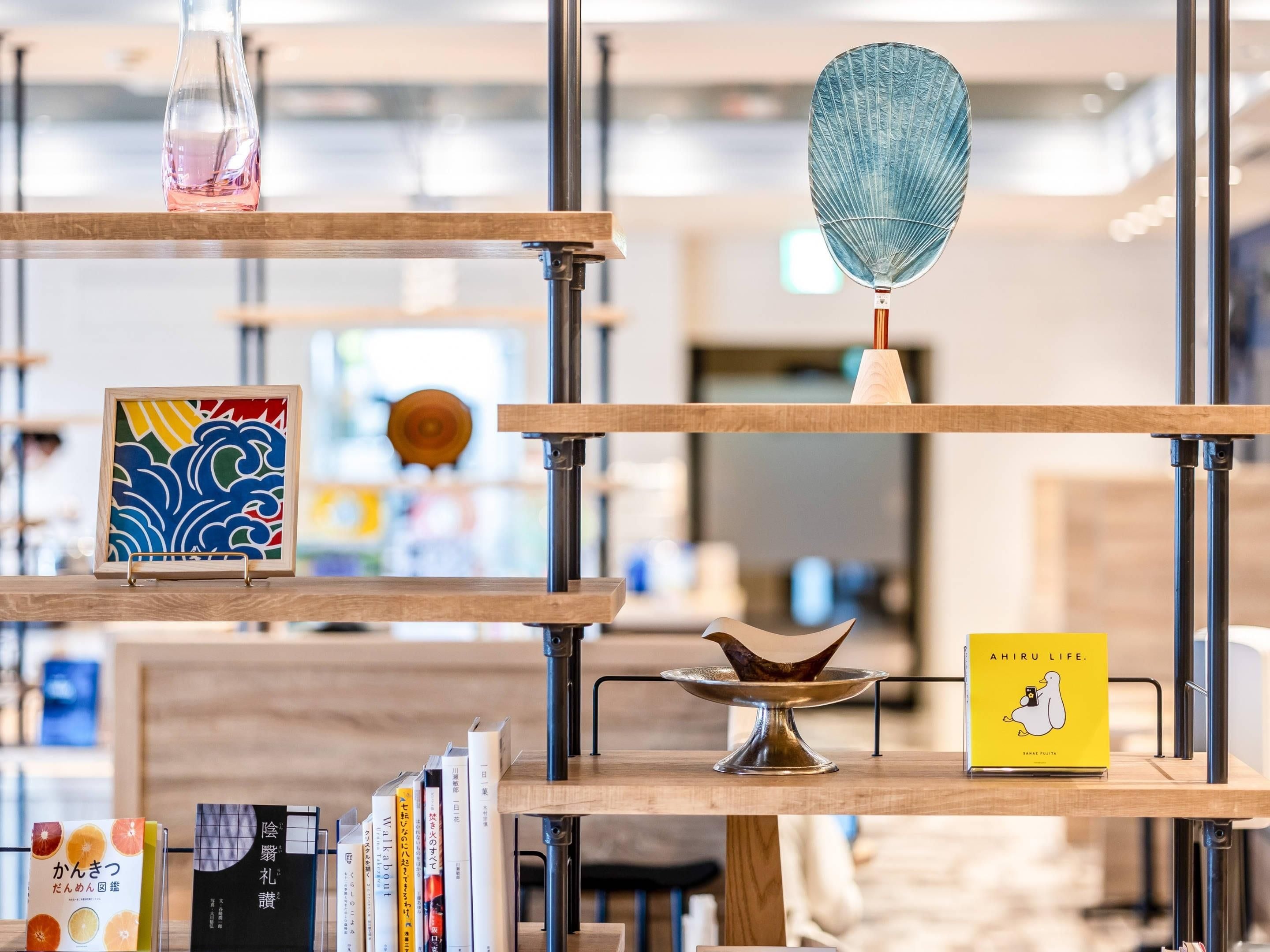 Una estantería de madera con varios niveles que contiene libros, un florero de vidrio y un cuenco decorativo.