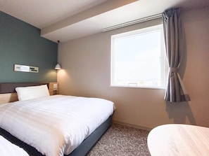 Habitación de hotel con cama, mesita de noche, ventana con cortinas y lámpara de pared.