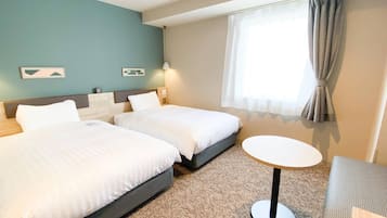 Quarto de hotel com duas camas, uma mesa redonda pequena e uma janela com cortinas.