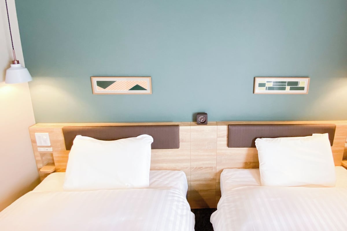 Habitación de hotel con dos camas, un cabecero de madera y dos relojes de pared.