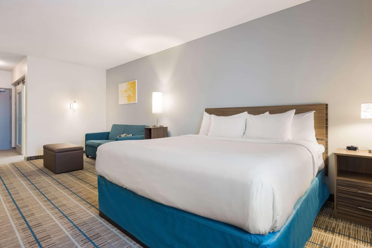 A hotel room with a large bed, a blue accent wall, a small seating area, and a nightstand with a lamp.