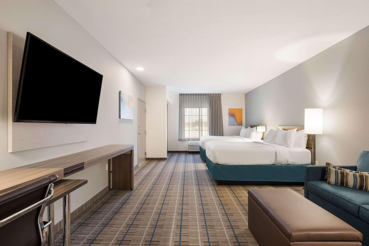 A hotel room with a flat-screen TV, a bed, a sofa, a desk, and a window with curtains.