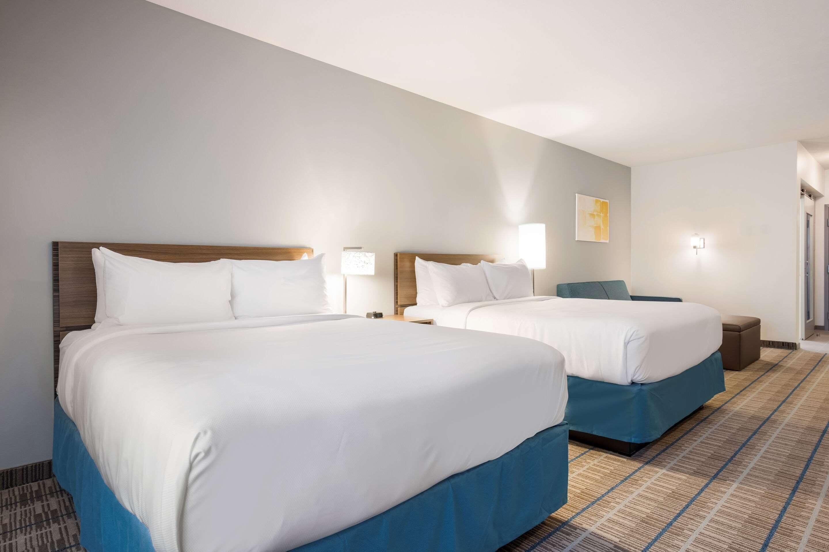 A hotel room with two beds, a nightstand, a lamp, a chair, and a carpeted floor.