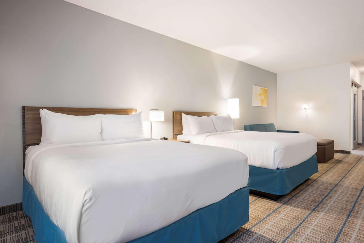 A hotel room with two beds, a nightstand, a lamp, a chair, and a carpeted floor.