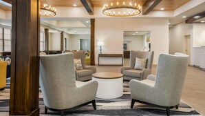 A modern lobby with grey armchairs, a round coffee table, and a reception desk. - MainStay Suites Gaylord (Gaylord)