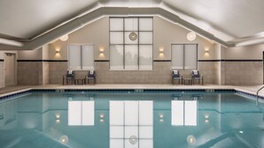 An indoor swimming pool with a high ceiling, recessed lighting, and a view through a large window. - MainStay Suites Gaylord (Gaylord)
