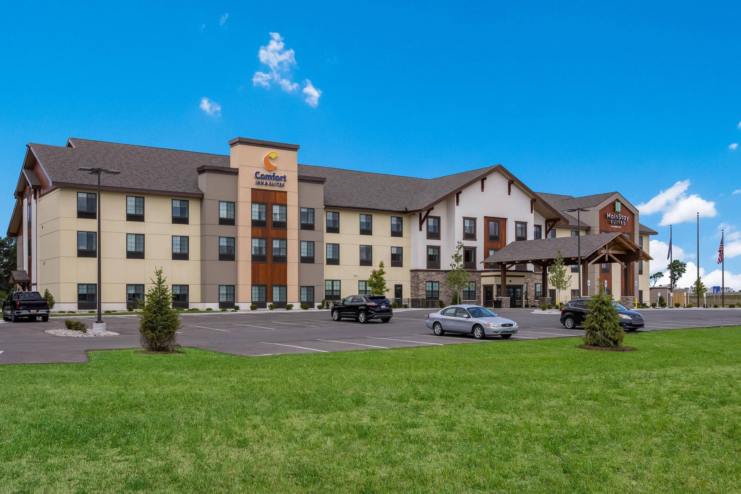 Un hôtel à plusieurs étages, avec une enseigne « Comfort Inn & Suites », une autre enseigne « Main Stay Suites » et un parking où sont garées plusieurs voitures.