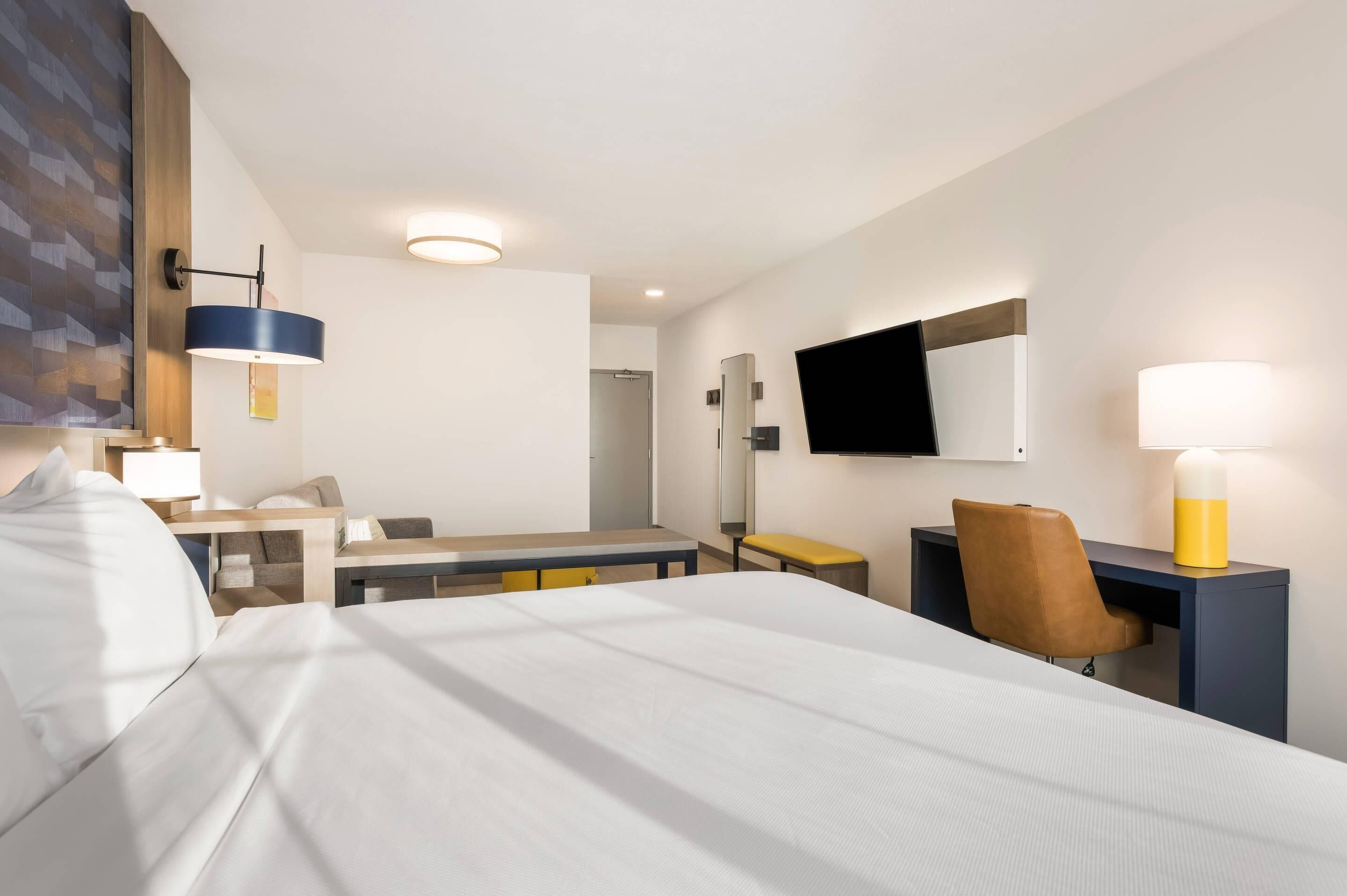 A hotel room with a bed, a desk, a chair, a television, and a bathroom.