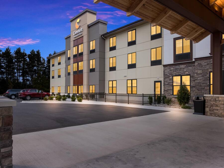 Un hotel de varios pisos con un letrero llamativo, un estacionamiento con automóviles y una entrada bien iluminada.