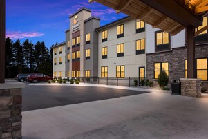 A multi-story hotel with a prominent sign, a parking area with cars, and a well-lit entrance.