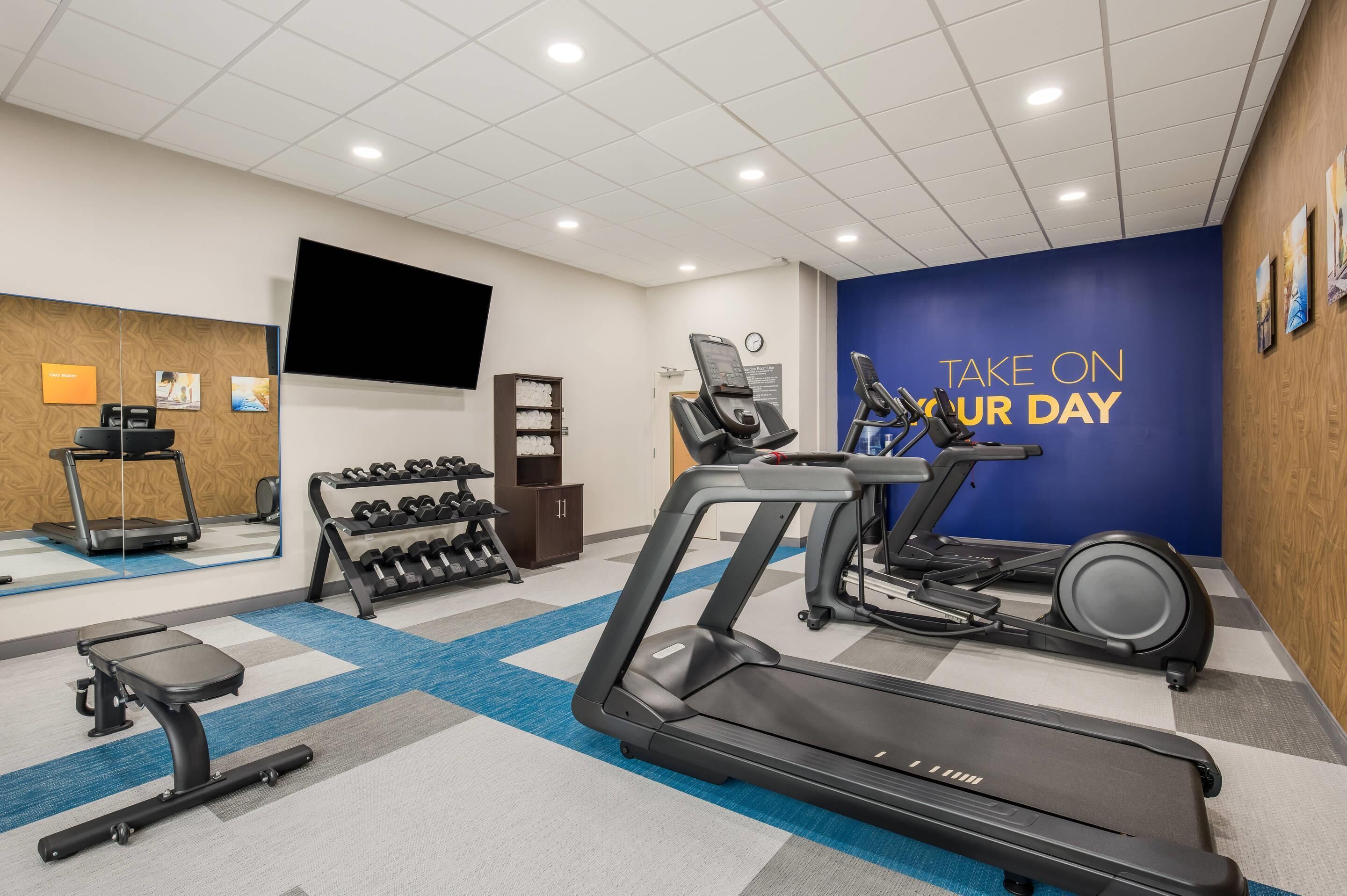 A gym with treadmills, dumbbells, and a wall with motivational text.