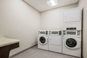 A laundry room with two front-loading washing machines and a table. - Comfort Inn & Suites Gaylord (Gaylord)