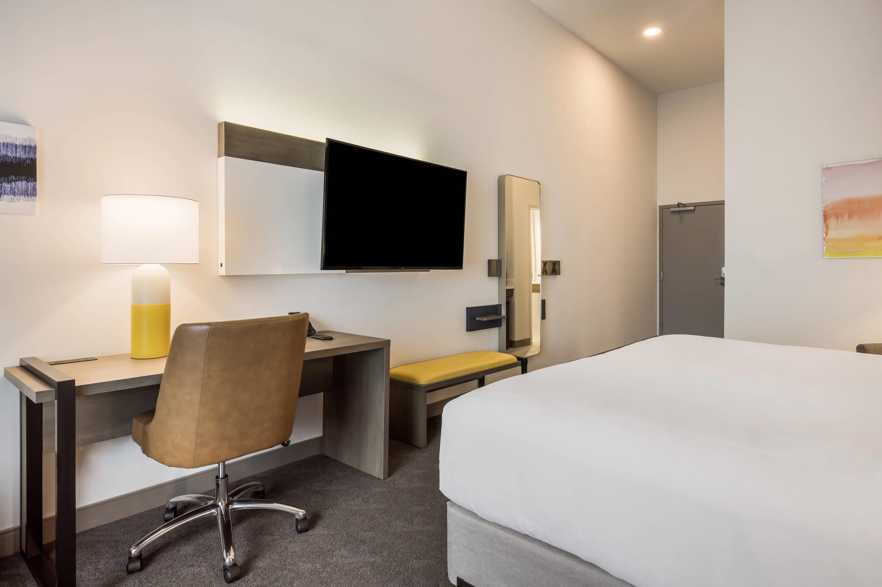 A hotel room with a bed, desk, chair, and a television.