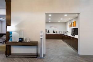 A modern reception area with a desk, a hand sanitizer dispenser, and a sign that reads 'RISE & SHINE'.