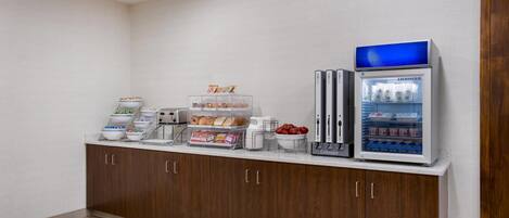 Una kitchenette con refrigerador, cafetera y una vitrina para pan.
