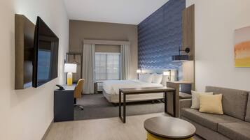 Habitación de hotel con cama, escritorio, silla, sofá, televisor y lámpara.