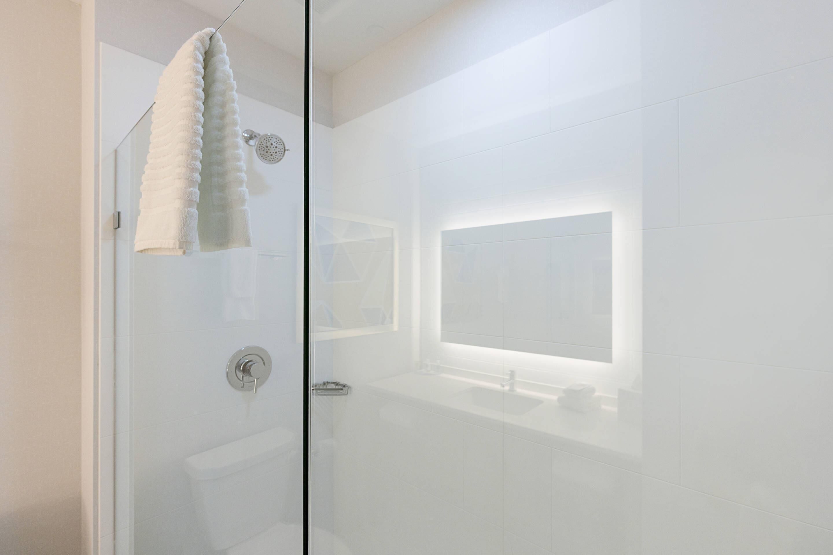 A modern bathroom with a glass shower enclosure, a visible towel, and a large mirror above the sink.