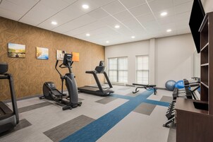 Un gimnasio con cintas de correr, elíptica, banco y pesas sueltas.