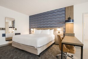 A hotel room with a bed, a desk, a chair, a mirror, and a wall with a geometric pattern.
