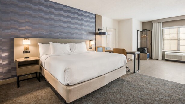 Une chambre d’hôtel avec un grand lit, un bureau, une chaise, une armoire et une fenêtre avec des rideaux.