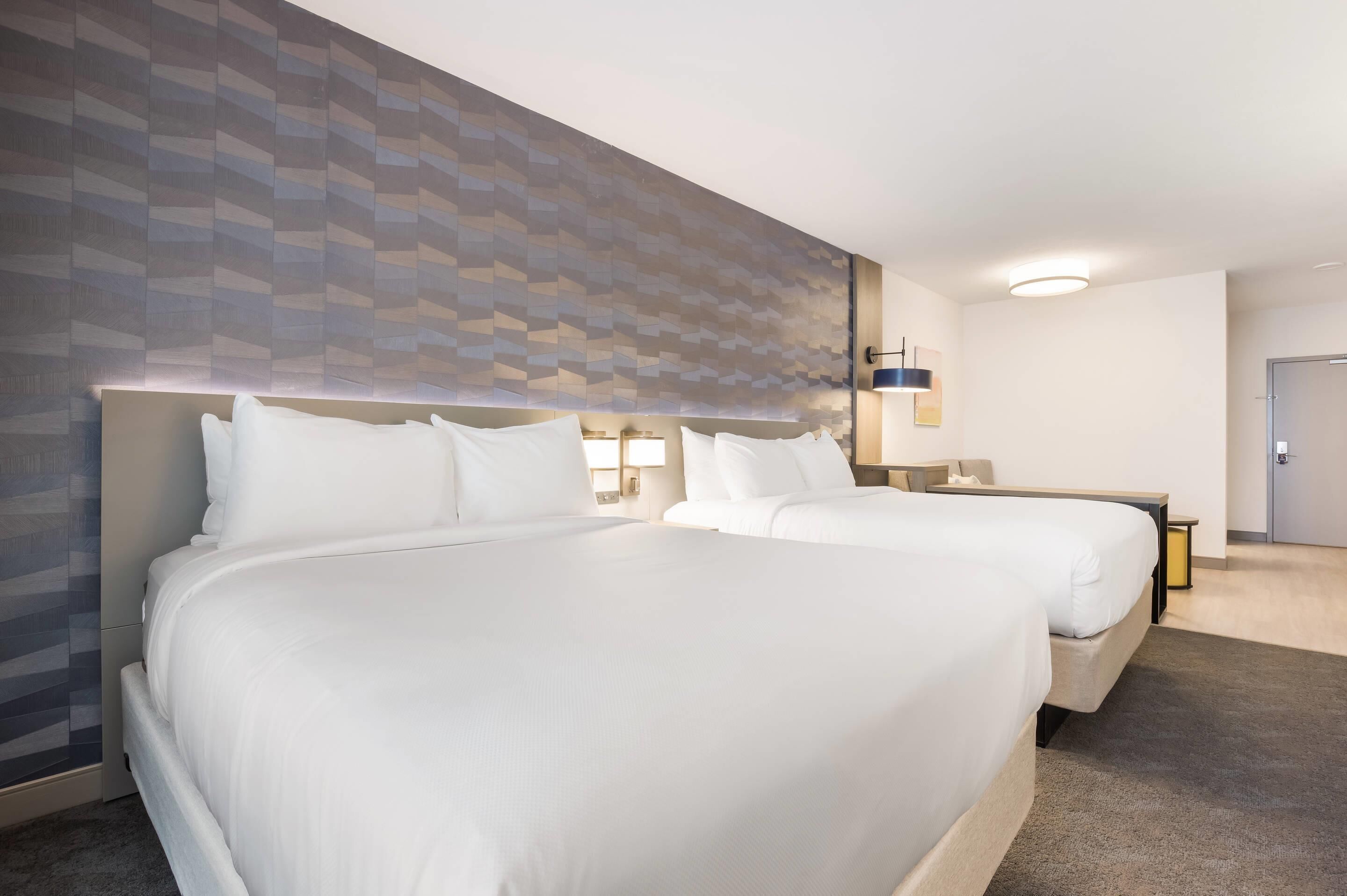 Ein Hotelzimmer mit zwei Betten, einem Wand-Fernseher, einem Nachttisch mit Lampe und einer Tür.
