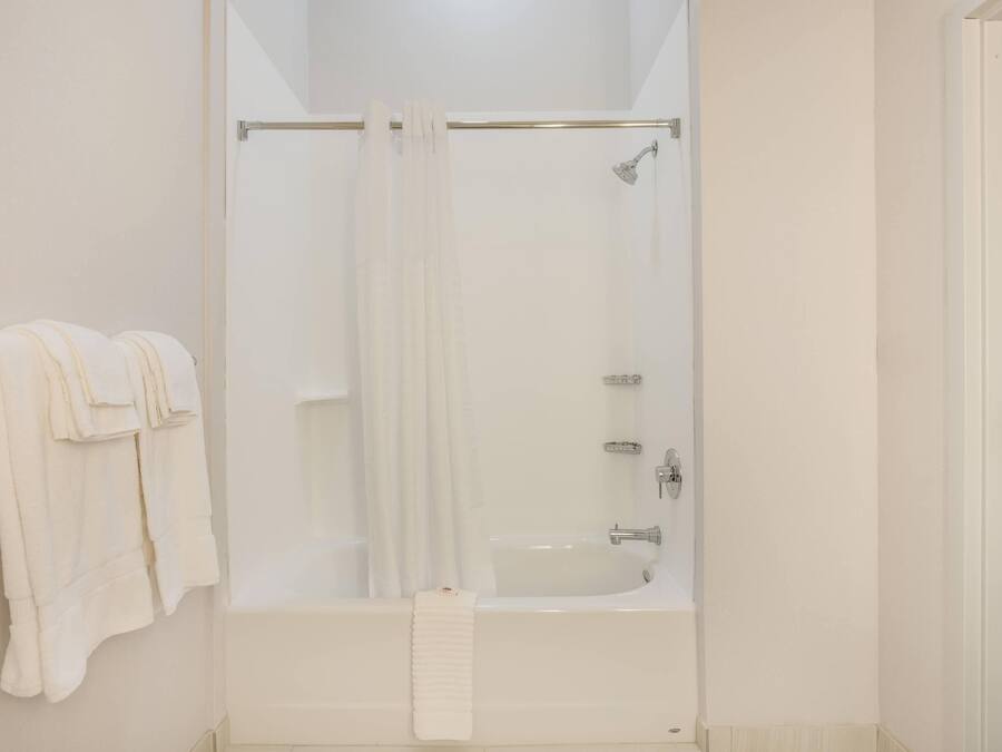 A bathroom with a glass-enclosed shower, a white bathtub, and a towel rack with folded towels.