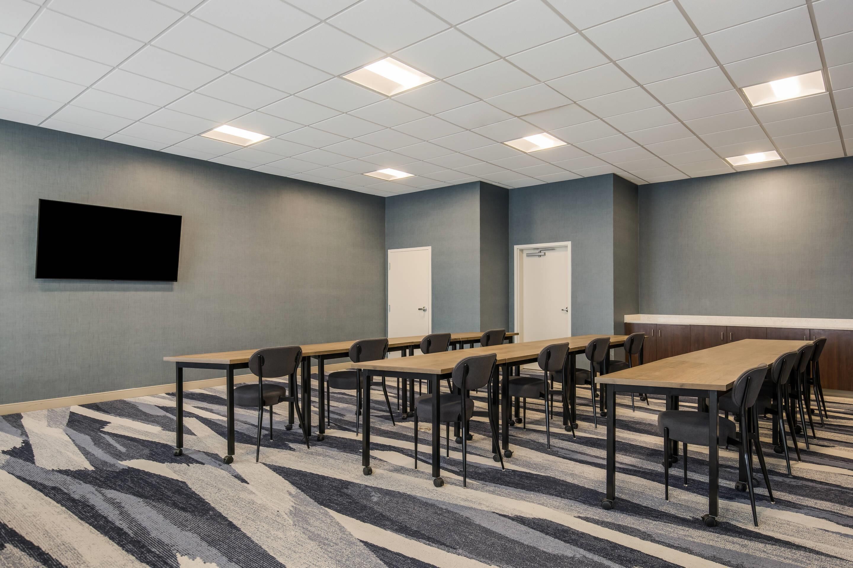 Une salle de conférence équipée d’une grande table, de chaises, d’un téléviseur à écran plat et d’un sol recouvert de moquette.