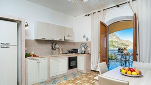 A kitchen with white cabinets, a tiled floor, and a view of a balcony with a table and chairs. - Waterfront apartment with beach access (Santa Flavia)