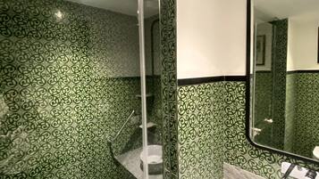 Een badkamer met groene betegeling, een douchecabine van glas, een witte wastafel en een spiegel.